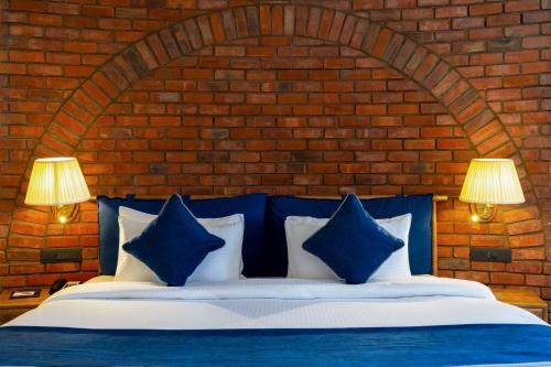 a bed with blue and white pillows in front of a brick wall at Ramee Royal Resort & Spa - Udaipur in Udaipur