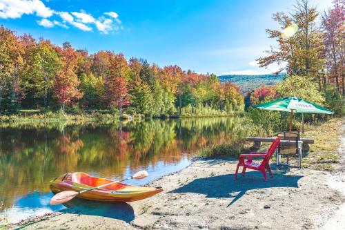 a picnic table and a chair and an umbrella next to a lake at paradis sauvage geronimo in St-Etienne de Bolton