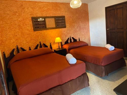 two beds in a room with orange walls at Hotel Posada San Pedro in Antigua Guatemala