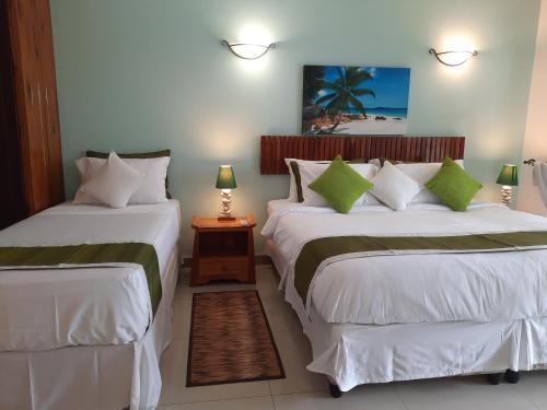 a bedroom with two beds with white sheets and green pillows at Cabanes Des Anges in La Digue