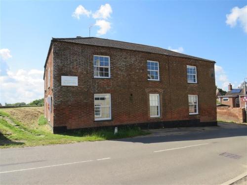 an old brick building on the side of a road at Riverbank Guest House in Wiggenhall Saint Germans