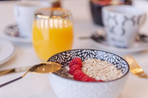a bowl of cereal and berries with a glass of orange juice at The Originals Boutique, Hôtel Porte de Dieppe in Saint-Aubin-sur-Scie