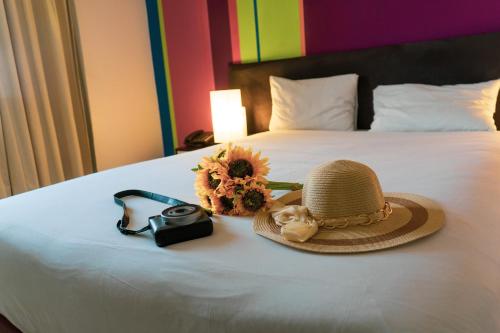 a hat and a camera and a sunflower on a bed at Ibis Styles Accra Airport in Accra