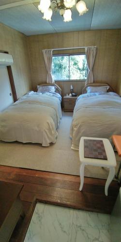 a bedroom with two beds and a table and a window at 田舎の宿 吉田屋 in Ōgo