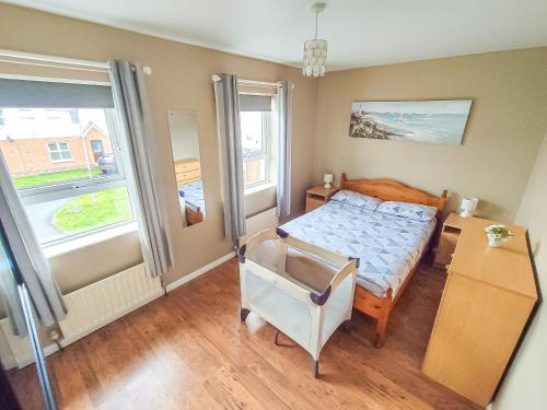 a bedroom with a bed and a desk and two windows at Portrush Getaway - Holiday Let in Portrush