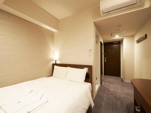 um quarto de hotel com uma cama com lençóis brancos em Sotetsu Fresa Inn Tokyo Roppongi em Tóquio