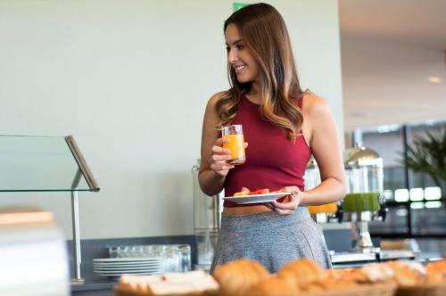 a woman holding a plate of food and a glass of orange juice at Staybridge Suites - Guadalajara Novena by IHG in Guadalajara