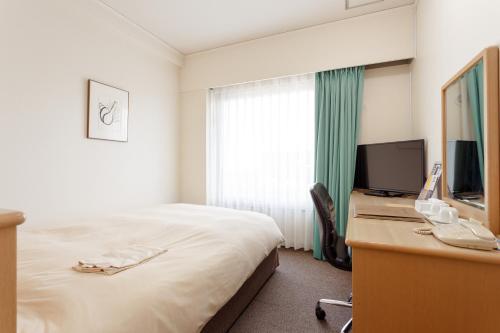 Habitación de hotel con cama y escritorio con TV. en AkishimaStationHotel TOKYO, en Akishima
