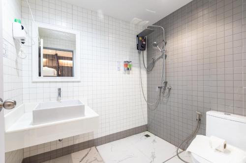 a white tiled bathroom with a sink and a shower at Baan Kun Mhor Hostel บ้านคุณหมอโฮสเทล in Bangkok