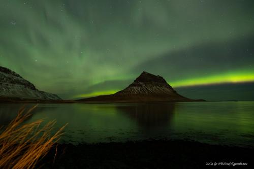 an aurora over a body of water with a mountain at Hellnafell in Grundarfjordur