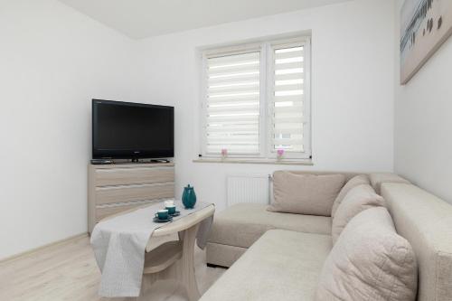 a white living room with a couch and a tv at Apartamenty Paryska by Renters in Kołobrzeg