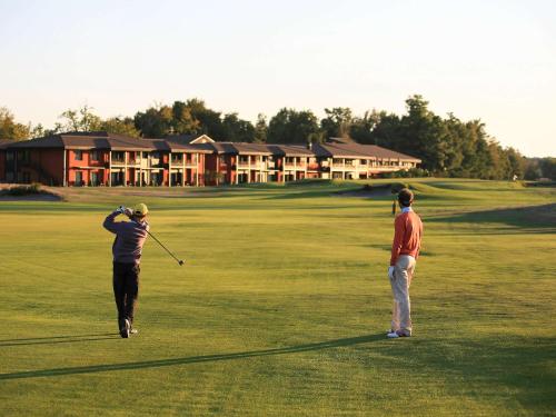 two men are playing golf on a golf course at Cabot Hotel Bordeaux - MGallery Collection in Le Pian-Médoc