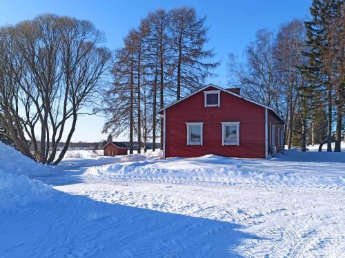 a red barn in a snow covered field with trees at Laukkumäki farm in Iisalmi