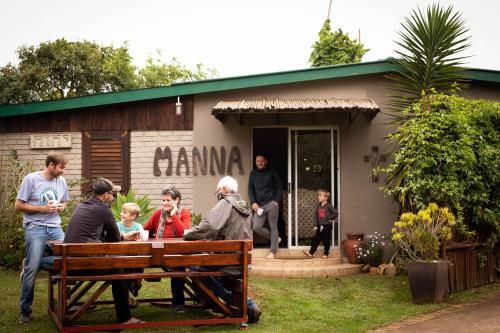 um grupo de pessoas em pé em torno de um banco em frente a uma casa em Manna Self Catering Guesthouse em Graskop