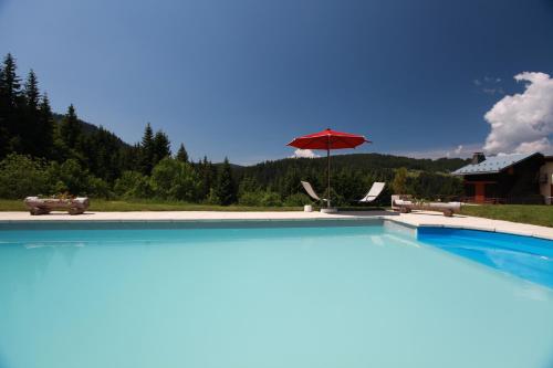 - une piscine avec un parasol rouge et une chaise dans l'établissement Hotel Le Tetras, à Notre-Dame-de-Bellecombe