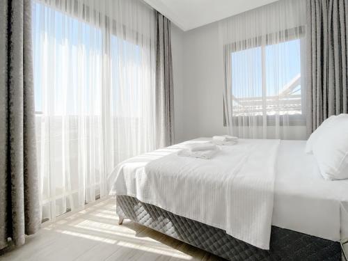 a white bedroom with a bed and a large window at Azize Palas Apart Otel in Çeşme