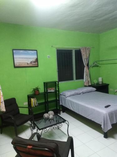 a bedroom with green walls and a bed and a chair at Casa Roja Áabilo'ob in Progreso