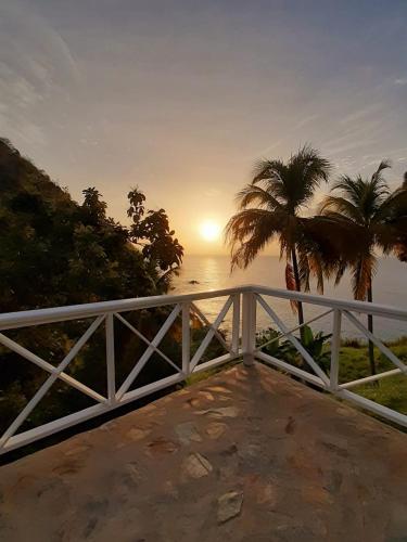 a sunset over the ocean with a white fence and palm trees at Castara Inn in Castara