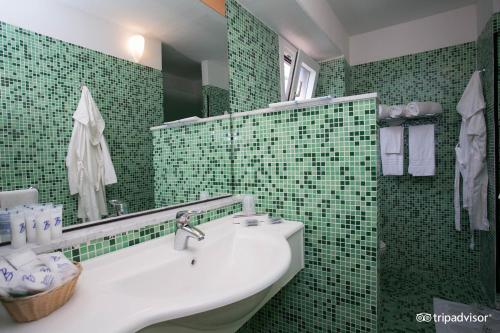 uma casa de banho com azulejos verdes, um lavatório e um espelho. em Villaggio Albatros Resort em Lesina