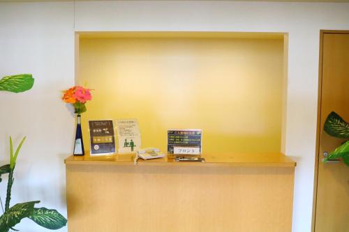a reception desk with a yellow wall and flowers at Hotel 4Season in Miyazaki
