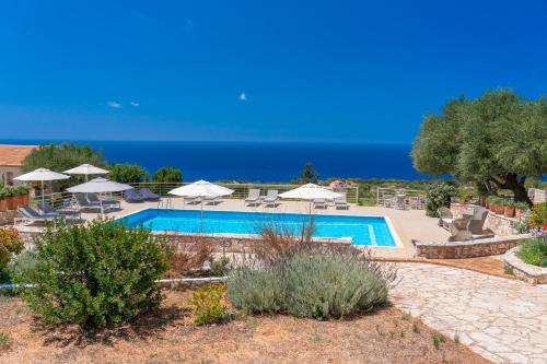 a pool with chairs and umbrellas and the ocean at Blue Horizon Cottages in Tzamarelláta