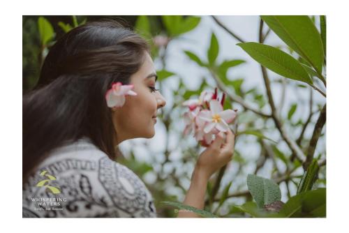 a young woman smelling a pink flower at Whispering Waters in Malayāttūr