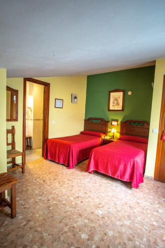 a bedroom with two beds with red sheets at Hotel Arunda II in Ronda