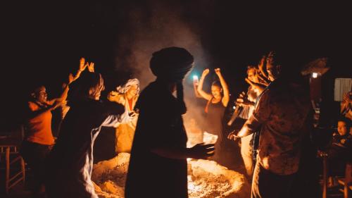 a group of people standing around a bonfire at Kam Kam Dunes in Merzouga
