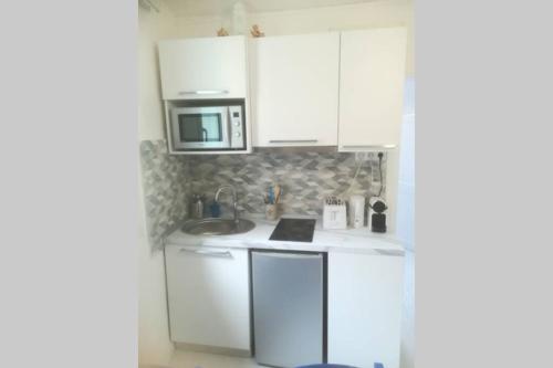 une cuisine blanche avec un évier et un micro-ondes dans l'établissement T2 à Menton Vue mer proche Plage, à Menton