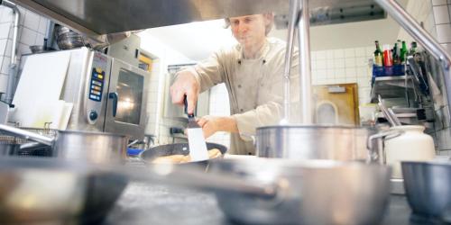 a chef stirring a pan in a kitchen at Hotel & Restaurant Zur Glocke in Höchstädt an der Donau