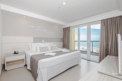 a white bedroom with a large bed and a large window at Guarujá Vivah in Guarujá