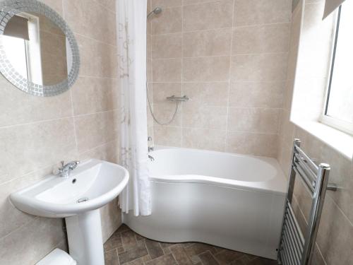 a bathroom with a sink and a bath tub and a mirror at Dunromin in Llandudno