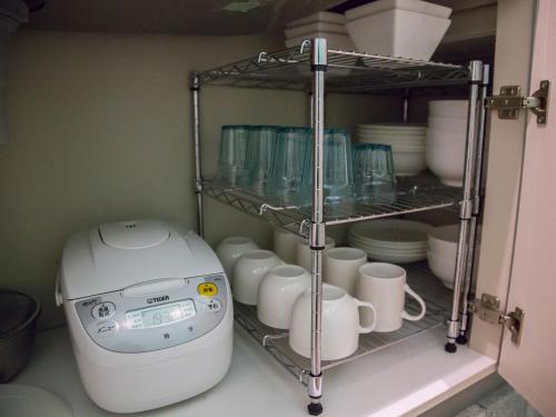 a coffee maker and cups on a shelf in a kitchen at Seawall Hostel in Chatan