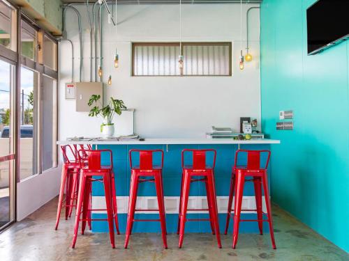 a kitchen with red stools in front of a blue counter at Seawall Hostel in Chatan