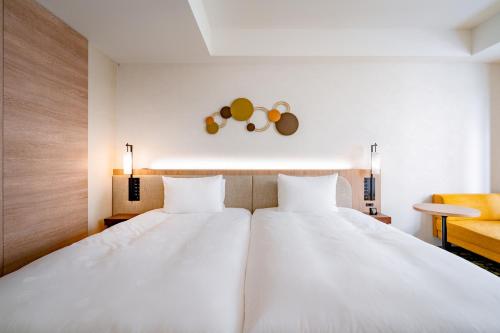 two white beds in a room with a yellow chair at The Royal Park Canvas - Kobe Sannomiya in Kobe