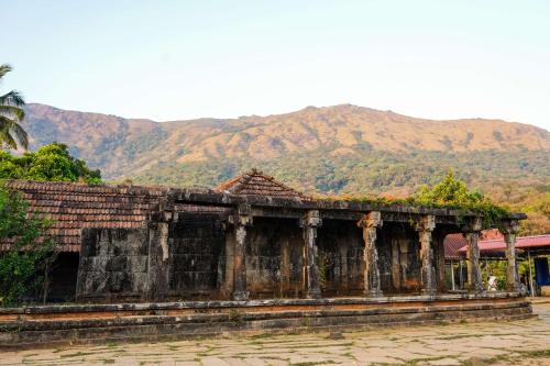 an old building with mountains in the background at Agraharam Resorts in Thirunelli
