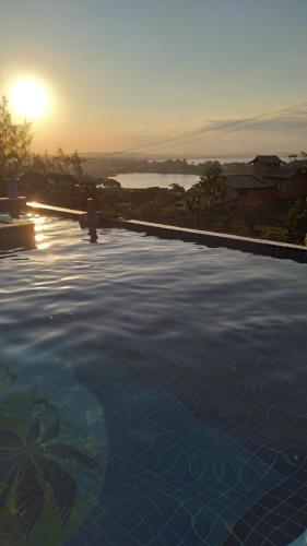 a large swimming pool with the sunset in the background at Hotel Pousada Casacolina in Búzios