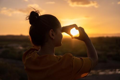 a woman making a heart shape with the sunset in the background at Regenbogen Properties - Salgados Vila das Lagoas in Albufeira