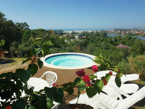 una piscina en una terraza con sillas blancas y flores en Chalés e Bangalôs Ibiraquera, en Praia do Rosa