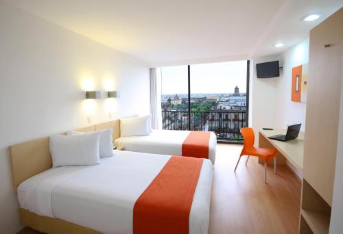 a hotel room with two beds and a desk and a window at One Guadalajara Centro Historico in Guadalajara