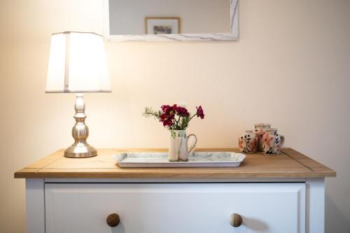 una mesa con una lámpara y un jarrón de flores. en Mill Cottage en Forres