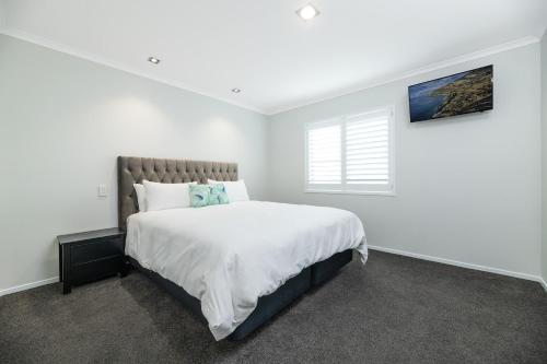 a white bedroom with a large bed and a window at Modern Marine Parade Apartment in Mount Maunganui
