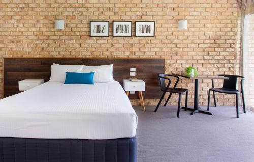 a bedroom with a bed, chair, desk and a lamp at Sunshine Coast Motor Lodge in Woombye