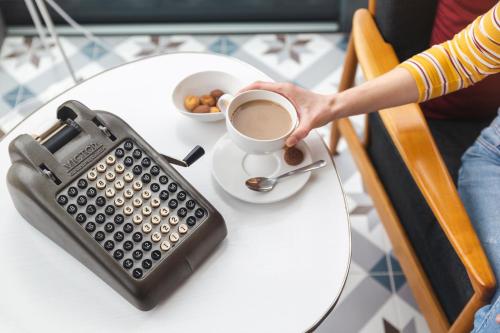 a person holding a cup of coffee next to a typewriter at Herdade do Ananás in Ponta Delgada