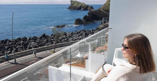 a woman sitting on a balcony looking at the ocean at Garoupas Inn in Ponta Delgada