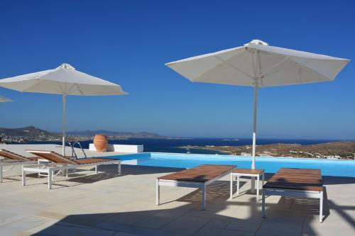 ein Swimmingpool mit zwei Sonnenschirmen und Stühlen und ein Swimmingpool in der Unterkunft White Blue Houses & Apartments Paros in Parikia