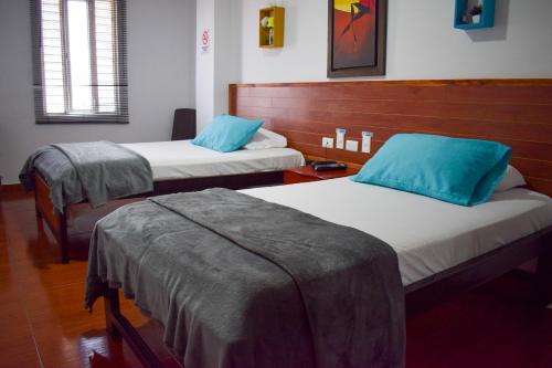 Dos camas en una habitación con almohadas azules. en Hotel Brisas De Calima en Cali