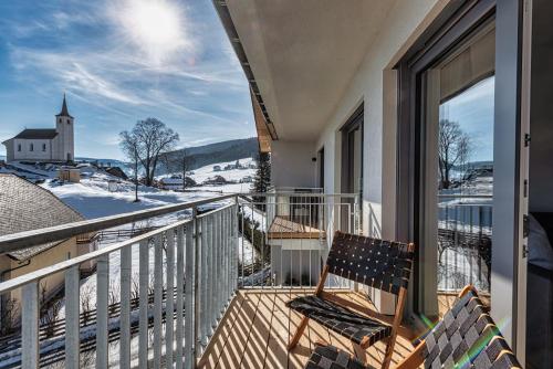 a balcony with a bench and a church in the snow at Ski & Nature Apartment in Mauterndorf