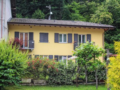 ein gelbes Haus mit schwarzen Fensterläden und Büschen in der Unterkunft Holiday Home Carmen by Interhome in Brissago Valtravaglia