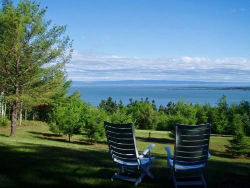two chairs sitting on a lawn with a view of the water at Chalet Sous Les Pins in Les Éboulements